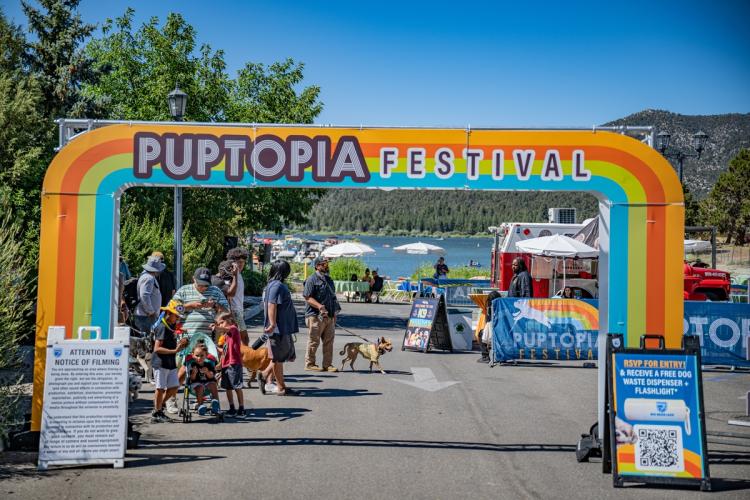Der Eingang zum Puptopia-Event mit Menschen und ihren Hunden im Hintergrund und dem See in der Ferne.