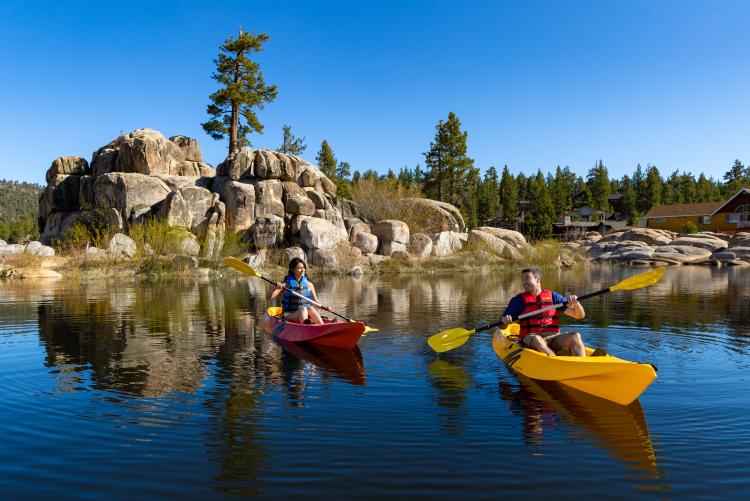 Ein Mann in einem gelben Kajak und eine Frau in einem roten Kajak auf dem Big Bear Lake an einem sonnigen Sommertag