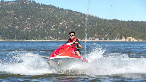 Eine Person in einer Schwimmweste fährt auf einem roten Jetski über ein Gewässer, das im Sommer im Big Bear Lake, Kalifornien, Wellen schlägt.