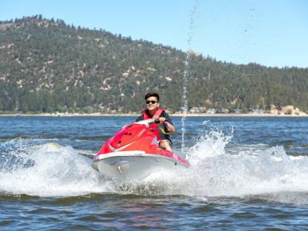 Eine Person in einer Schwimmweste fährt auf einem roten Jetski über ein Gewässer, das im Sommer im Big Bear Lake, Kalifornien, Wellen schlägt.