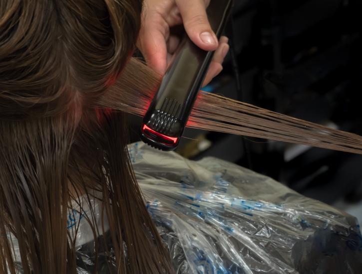 Ein Foto einer Dame, die sich in einem Friseursalon mit einer Heizwalze die Haare stylen lässt.