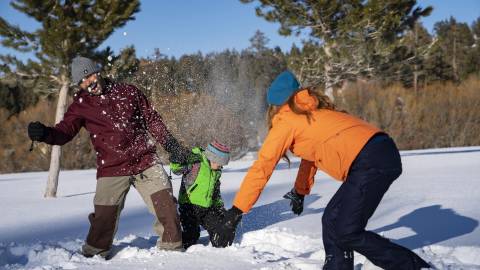 Eine dreiköpfige Familie spielt im Winter am Big Bear Lake im Schnee.