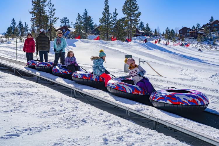 Eine Familie fährt auf einem fahrenden Teppich zum Schneespiel in Big Bear. Sie tragen bunte Schneeschläuche.