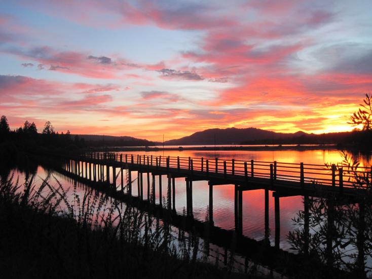 Ein farbenfroher Sonnenuntergang am Big Bear Lake mit Rot-, Violett- und Gelbtönen am Himmel über einer schwarzen Silhouette des Boardwalk.