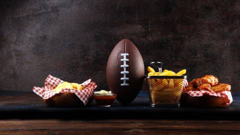 Ein Fußball liegt auf einem Holztisch mit Pommes frites und Hähnchenflügeln als Vorspeise. Archivbild.