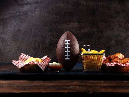 Ein Fußball liegt auf einem Holztisch mit Pommes frites und Hähnchenflügeln als Vorspeise. Archivbild.