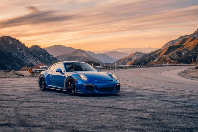 Ein blauer Porsche steht am Straßenrand einer kurvenreichen Bergstraße. Werbung für die Porsche Timeline-Veranstaltung in Big Bear Lake.