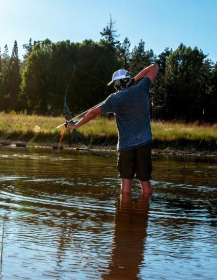 Ein Mann mit blauem Hemd und weißer Mütze watet im Wasser und zielt während der Countin' Carp-Veranstaltung mit seinem Bogen auf das Wasser.