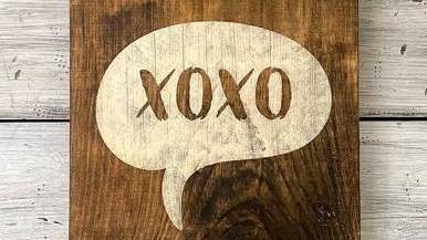 Ein hölzernes Schild mit der Aufschrift XOXO steht auf einem weißen Hintergrund.