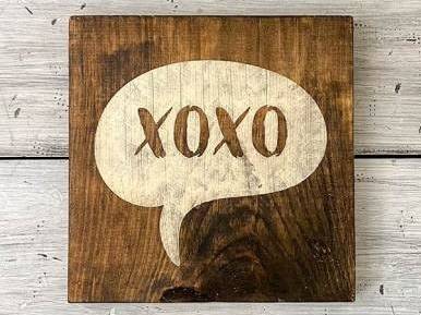 Ein hölzernes Schild mit der Aufschrift XOXO steht auf einem weißen Hintergrund.
