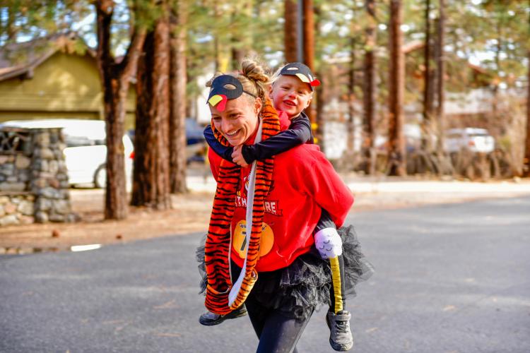 Ein Foto einer Mutter mit einer Truthahnmaske, die ihr Kind während des Thanksgiving Turkey Trot auf dem Rücken trägt