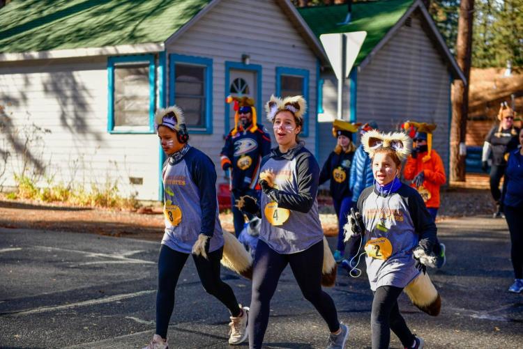 Eine Gruppe von drei Mädchen, die am Thanksgiving Turkey Trot teilnehmen. Sie tragen Gesichtsbemalung und sind als Fennec-Füchse verkleidet.