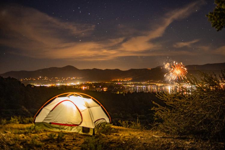 Ein beleuchtetes Campingzelt auf einem Hügel mit Blick auf Big Bear und das Feuerwerk zum 4. Juli