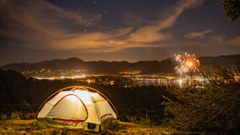Ein beleuchtetes Campingzelt auf einem Hügel mit Blick auf Big Bear und das Feuerwerk zum 4. Juli