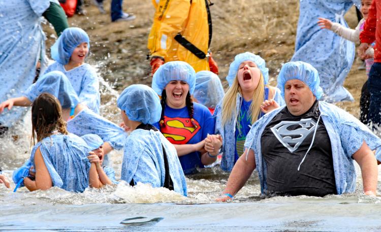 Eine Gruppe von Männern und Frauen trägt Krankenhauskittel und -mützen, als sie während des Big Bear Polar Plunge in den Big Bear Lake eintauchen.