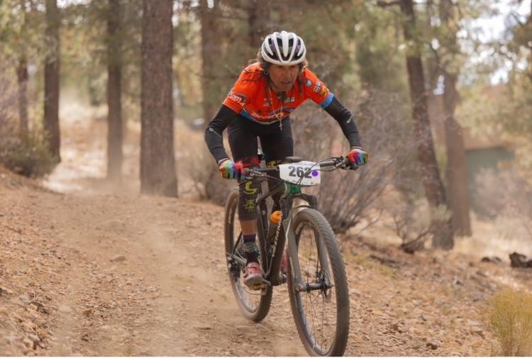Ein Foto von einer Mountainbikerin, die auf einem unbefestigten Weg in Richtung des Betrachters fährt und dabei eine Staubspur hinter sich herzieht.