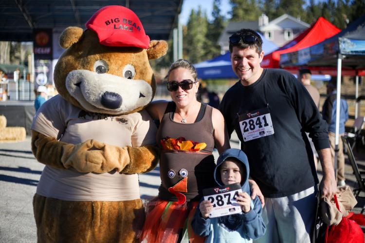 Eine Mutter, ein Vater und ein Kind lächeln für ein Foto mit dem Maskottchen des Big Bear Turkey Trot während des Big Bear Turkey Trot.