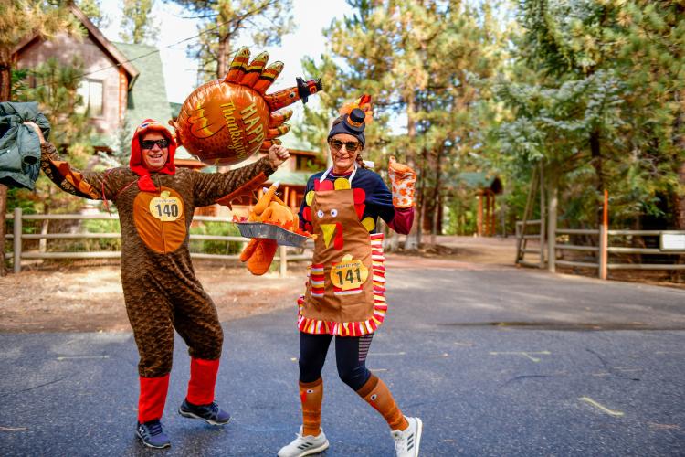 Ein Foto von einem Paar in ihren Truthahnkostümen während des Thanksgiving Turkey Trot, die Dame hält einen falschen Truthahnbraten.