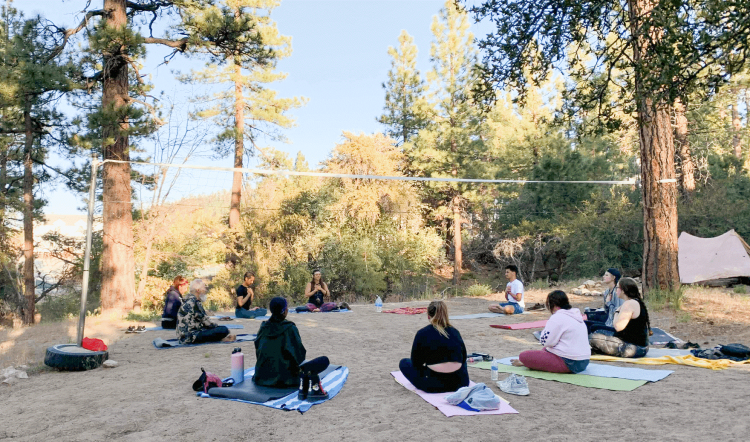 Eine kleine Gruppe hält einen Yogakreis in den Waldbergen, sie sitzen auf Handtüchern im Schatten.