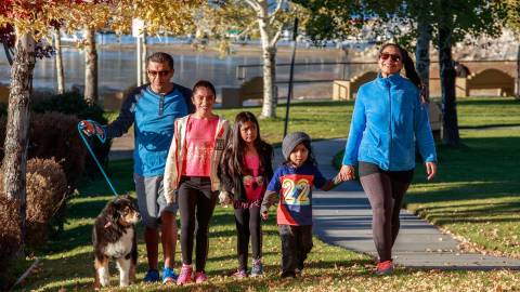 Eine fünfköpfige Familie mit drei kleinen Kindern und einem Hund, die im Herbst im Park durch das Laub spaziert.