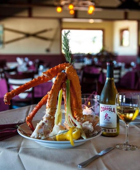 Ein Foto von einem Krabbenbeingericht in der Pines Lakefront Tavern, daneben eine Flasche Coppola Chardonnay und ein gefülltes Weinglas