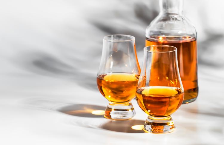 Eine Karaffe und zwei Gläser sind mit bernsteinfarbenem Bourbon gefüllt. Sie werfen Schatten und Reflektionen auf den weißen Hintergrund.