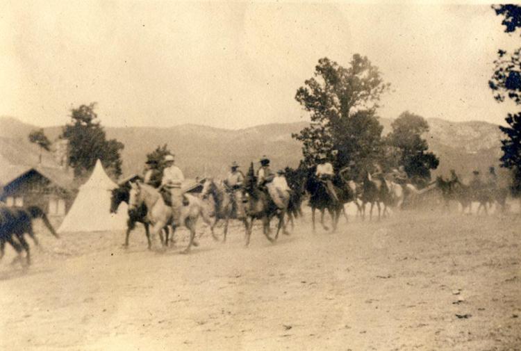 Ein altes Foto einer Gruppe von Männern auf Pferden im Big Bear Valley, hinter ihnen sind Häuser und Zelte zu sehen.