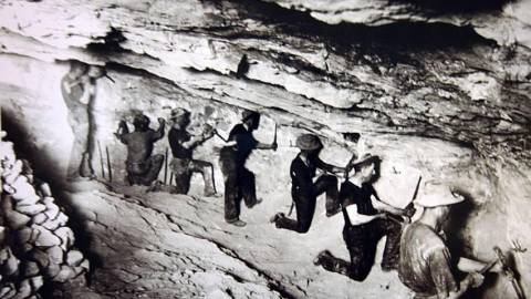 Ein Schwarz-Weiß-Foto von einer Gruppe von Goldsuchern, die in einer Höhle nach Gold suchen.