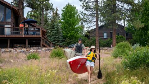Ein Paar trägt Paddelbretter von seinem Ferienhaus am See zum Big Bear Lake.