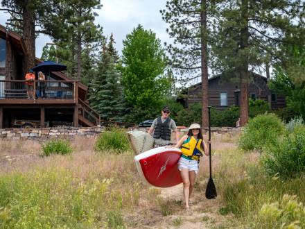 Ein Paar trägt Paddelbretter von seinem Ferienhaus am See zum Big Bear Lake.